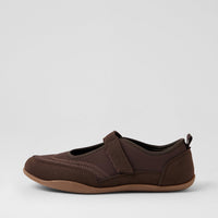 A dark brown slip-on shoe with a hook-and-loop strap closure and a tan outsole, shown in profile against a light gray background.
