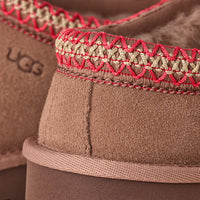 Close-up of brown UGG boots with red and gold stitching.