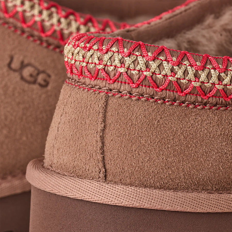 Close-up of brown UGG boots with red and gold stitching.