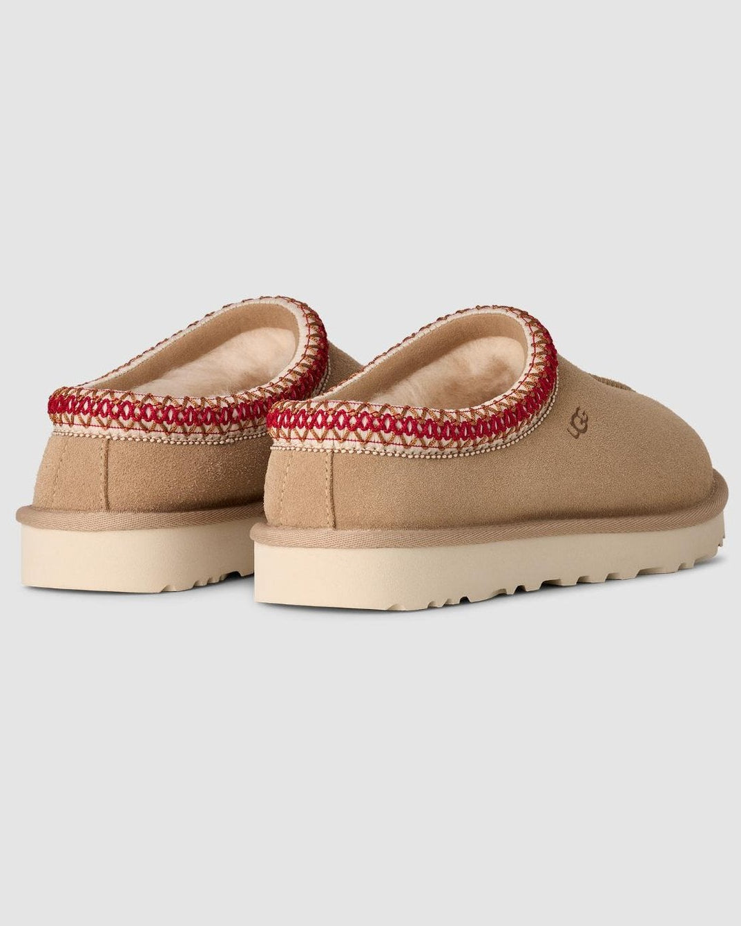 Pair of tan slippers with red trim on a light gray background