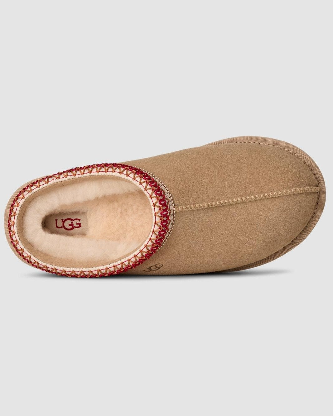 Tan UGG slipper with red trim on a light gray background