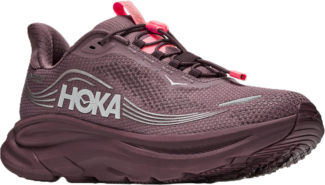 A HOKA trail running shoe in a dark plum purple colorway, featuring a textured mesh upper, a thick cushioned sole, and bright pink accents on the laces and tongue pull tab.