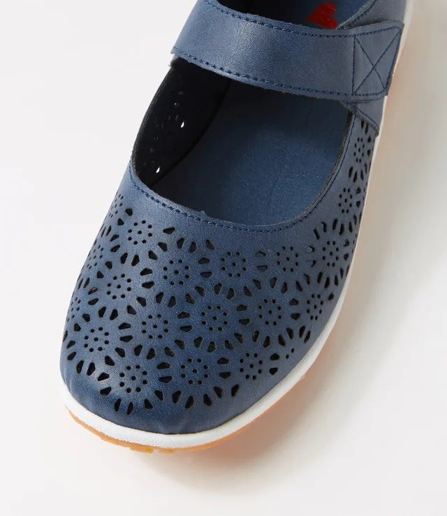 A close-up of a blue perforated Mary Jane shoe with a hook-and-loop strap, shown on a white background.