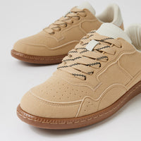 A pair of beige suede low-top sneakers with brown rubber soles and black-and-white patterned laces, shown on a clean white background.