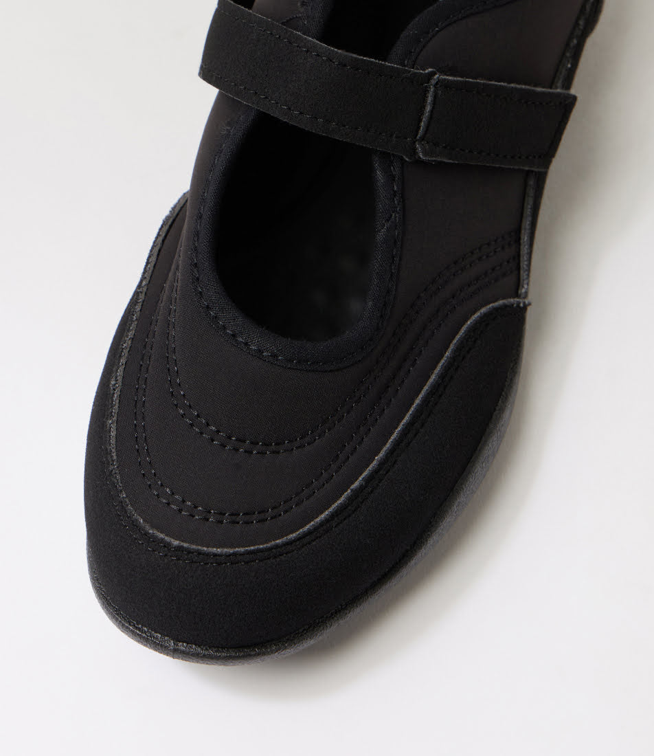 A close-up of a black Mary Jane style shoe with a hook-and-loop strap, photographed on a clean white background.