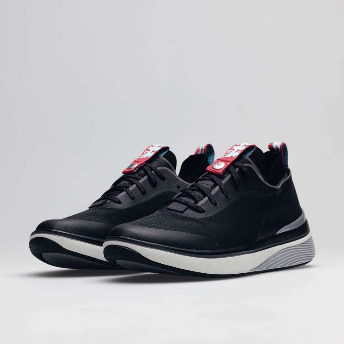 A pair of BALA Twelves in Nocturnal, which are premium, athletic-style sneakers for nurses and healthcare workers. The shoes have black uppers, white soles, and silver detailing around the heel, along with black laces and bright red and sky blue details o