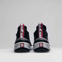 A pair of BALA Twelves in Nocturnal, which are premium, athletic-style sneakers for nurses and healthcare workers. The shoes have black uppers, white soles, and silver detailing around the heel. They are photographed from the back against a solid white background, showcasing bright red and sky blue details along the heel seam, including a rubber BALA logo inset in the sole.